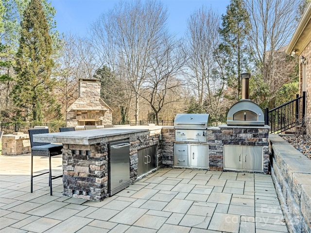 view of patio featuring a grill, exterior kitchen, a fireplace, and fence