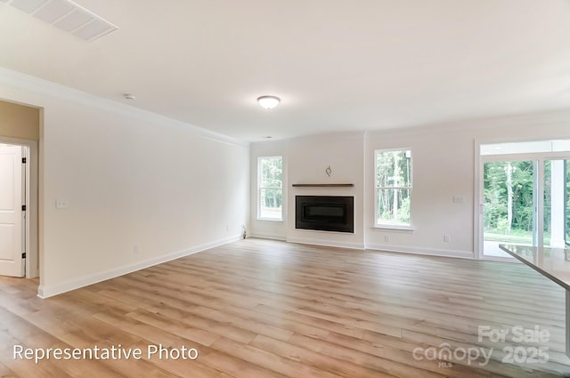 unfurnished living room with light wood finished floors, visible vents, a healthy amount of sunlight, and a glass covered fireplace