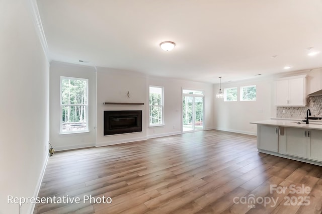 unfurnished living room with light wood finished floors, a glass covered fireplace, baseboards, and ornamental molding