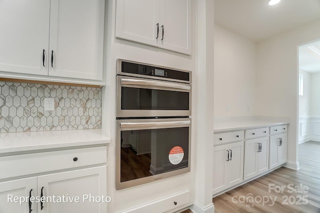 kitchen featuring decorative backsplash, white cabinets, double oven, and light countertops