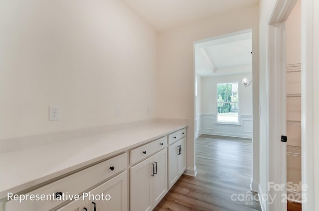 corridor featuring wood finished floors, wainscoting, and a decorative wall