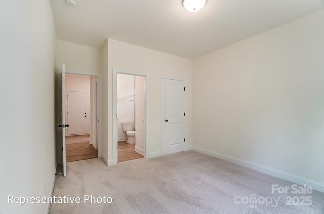 unfurnished bedroom with ensuite bath, baseboards, and carpet floors