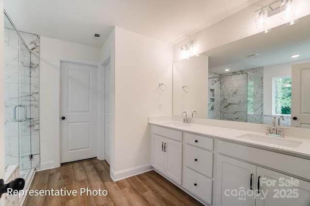 full bath featuring double vanity, wood finished floors, a marble finish shower, and a sink