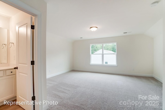 empty room featuring visible vents, baseboards, light colored carpet, and vaulted ceiling