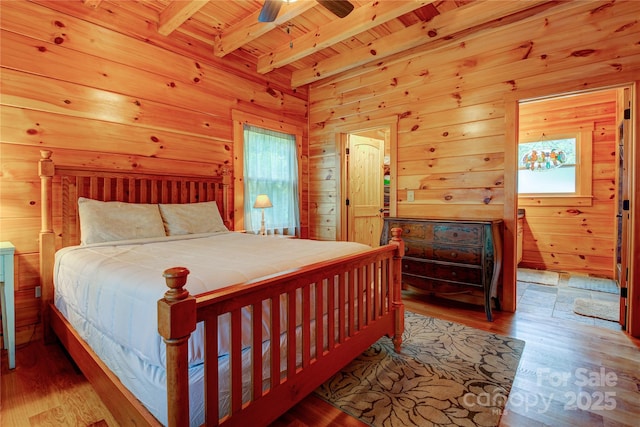 bedroom with beamed ceiling, a ceiling fan, wood finished floors, wood walls, and wooden ceiling