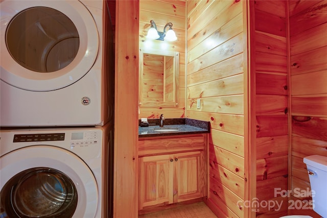 washroom featuring a sink, stacked washer and clothes dryer, wood walls, and laundry area