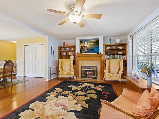 living room featuring a fireplace with flush hearth, a textured ceiling, ceiling fan, and wood finished floors