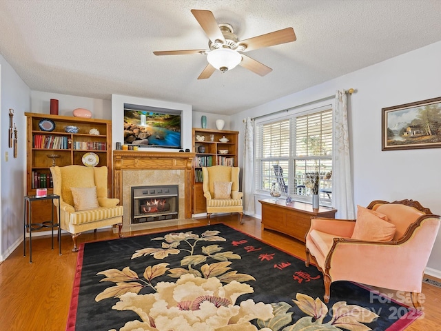 living area with a textured ceiling, wood finished floors, a ceiling fan, and a tile fireplace