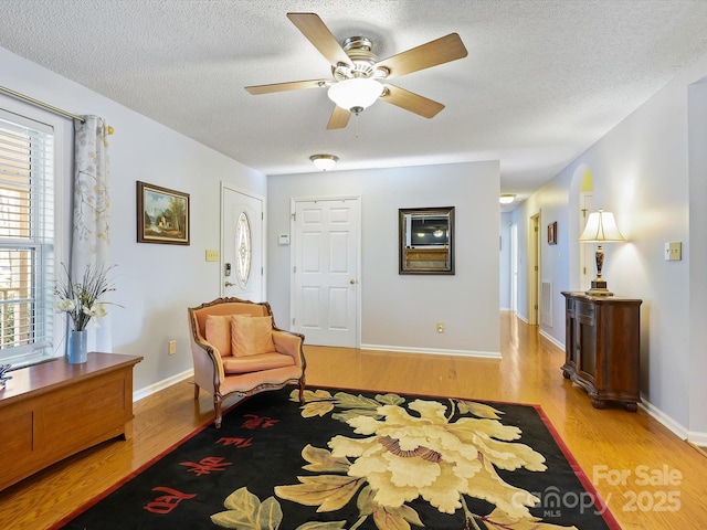 living area featuring visible vents, a textured ceiling, baseboards, and wood finished floors