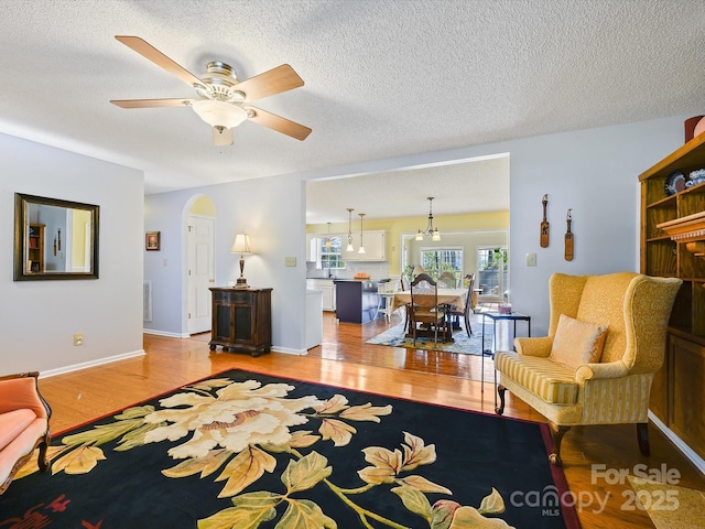 living area with arched walkways, light wood-style floors, ceiling fan, and a textured ceiling