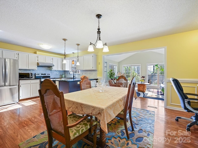 dining room featuring a wainscoted wall, visible vents, a textured ceiling, and light wood-style floors