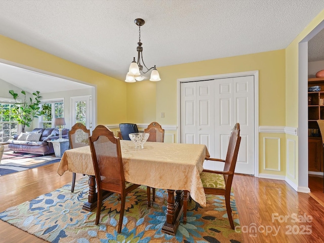 dining room featuring a textured ceiling, a notable chandelier, wood finished floors, and wainscoting