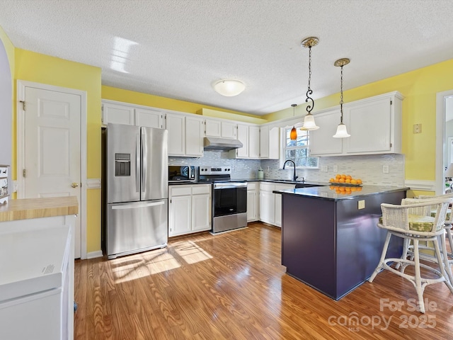 kitchen featuring under cabinet range hood, appliances with stainless steel finishes, a peninsula, light wood-style floors, and white cabinets