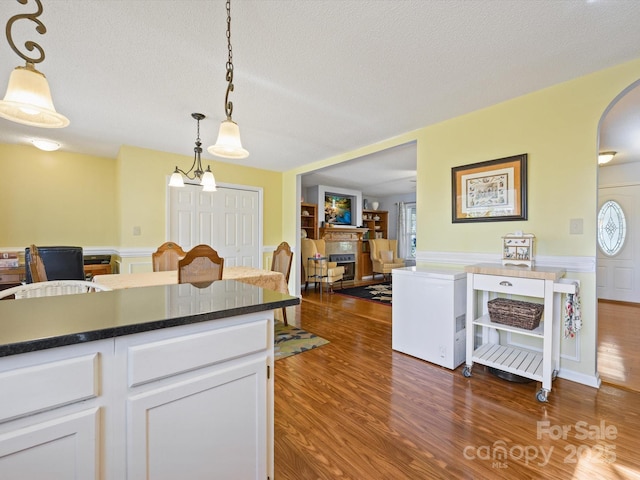 kitchen featuring decorative light fixtures, dark wood-style floors, a fireplace, arched walkways, and white cabinets