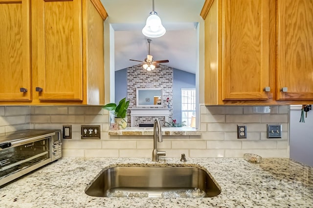 kitchen with vaulted ceiling, light stone counters, brown cabinets, a ceiling fan, and a sink