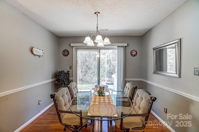 dining room featuring baseboards, wood finished floors, a textured ceiling, and a chandelier