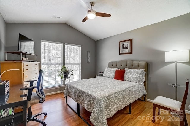 bedroom with a ceiling fan, wood finished floors, visible vents, baseboards, and vaulted ceiling