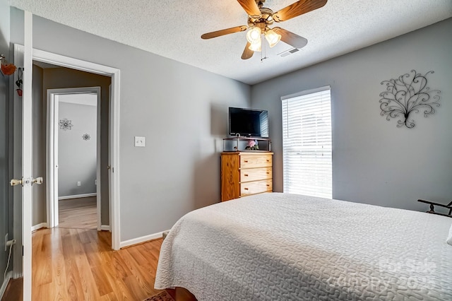 bedroom featuring visible vents, a ceiling fan, a textured ceiling, light wood-style floors, and baseboards