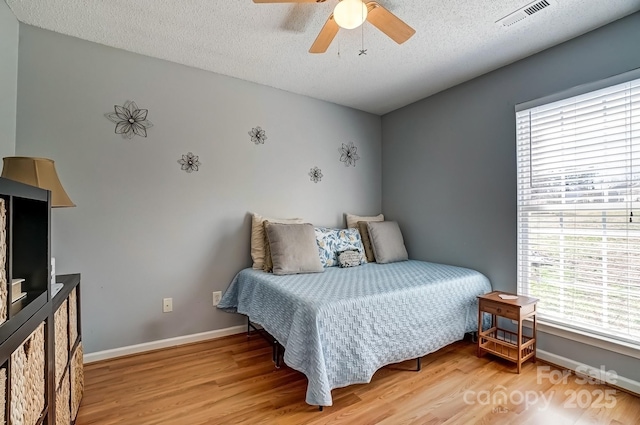 bedroom featuring baseboards, visible vents, light wood-style flooring, ceiling fan, and a textured ceiling