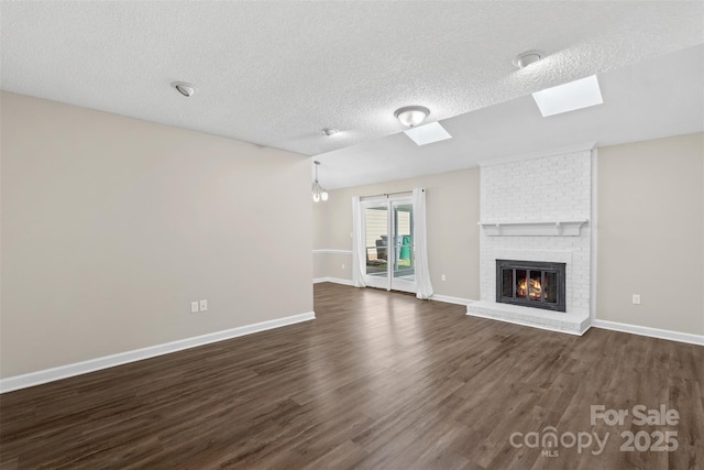 unfurnished living room with baseboards, dark wood-style flooring, a skylight, and a brick fireplace