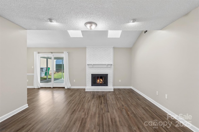unfurnished living room with dark wood finished floors, baseboards, a skylight, and a brick fireplace