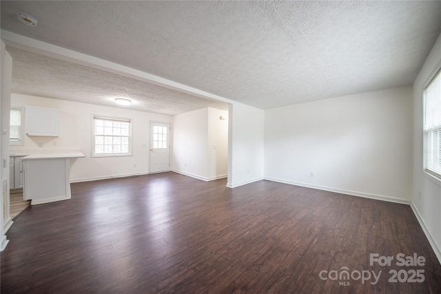 unfurnished living room with a textured ceiling, dark wood-type flooring, and baseboards