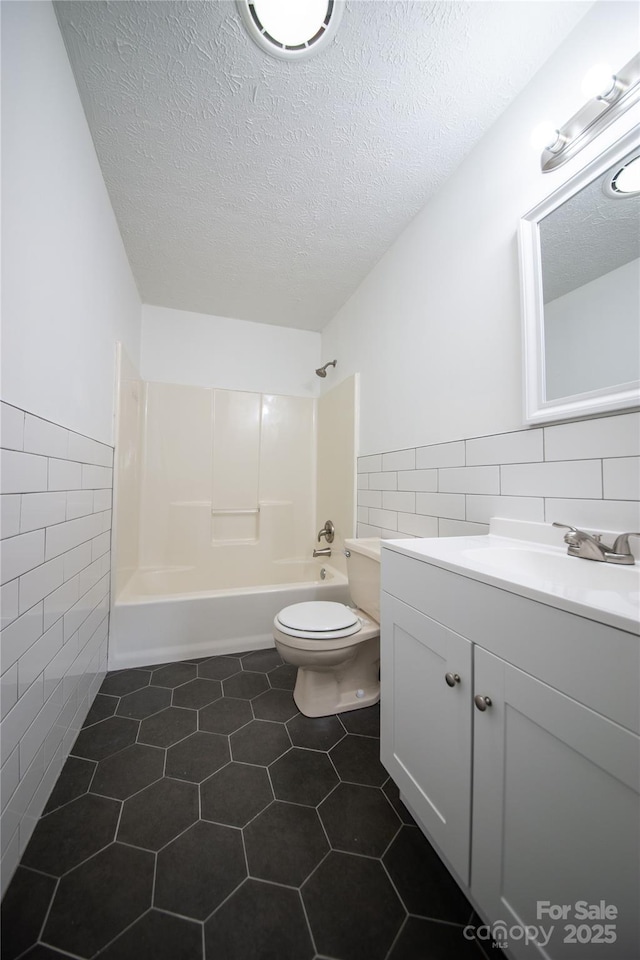 full bathroom featuring toilet, tile patterned flooring, a textured ceiling, vanity, and tile walls