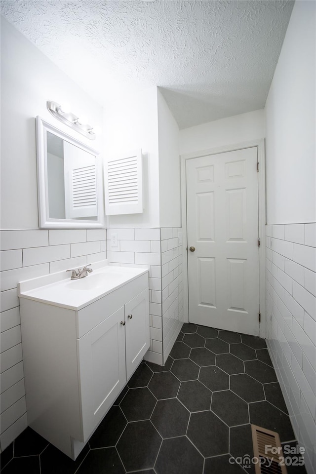 bathroom with a wainscoted wall, tile patterned flooring, a textured ceiling, and tile walls