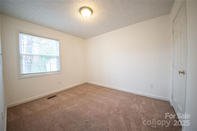 spare room with carpet floors, visible vents, a textured ceiling, and baseboards