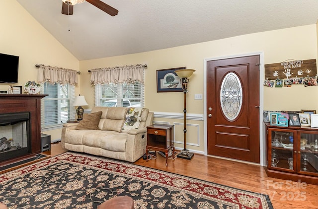 living area with lofted ceiling, a textured ceiling, a fireplace, wood finished floors, and a ceiling fan