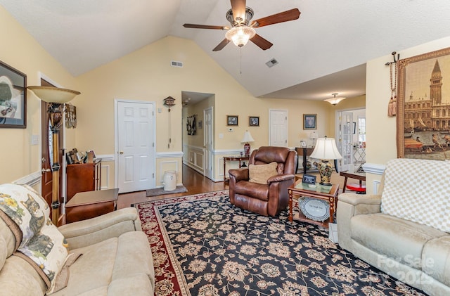 living area with visible vents, a ceiling fan, a wainscoted wall, wood finished floors, and vaulted ceiling