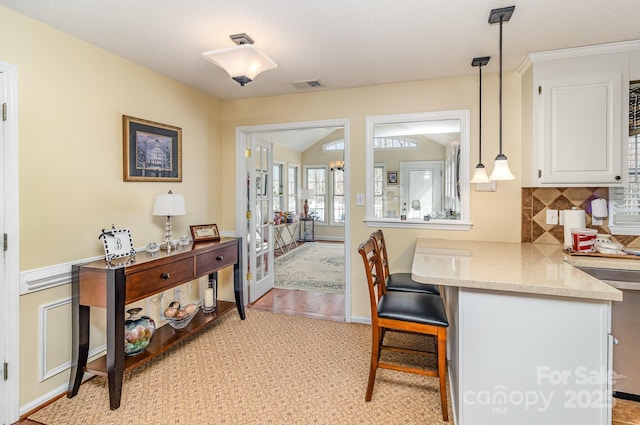 interior space featuring light stone counters, white cabinetry, visible vents, a kitchen breakfast bar, and decorative backsplash