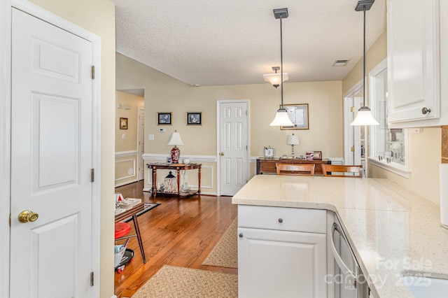 kitchen with wainscoting, white cabinetry, a textured ceiling, wood finished floors, and a peninsula