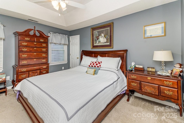 carpeted bedroom with a ceiling fan, visible vents, and a tray ceiling