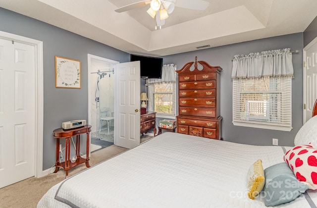 carpeted bedroom with ceiling fan, ensuite bath, a raised ceiling, and visible vents