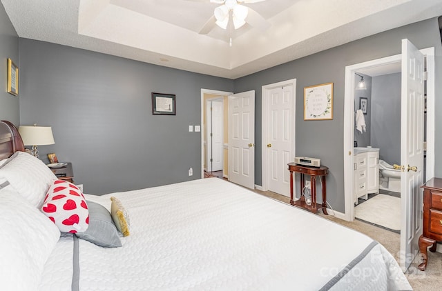 bedroom with ceiling fan, connected bathroom, light carpet, baseboards, and a tray ceiling