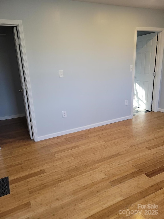 spare room featuring light wood-type flooring, visible vents, and baseboards