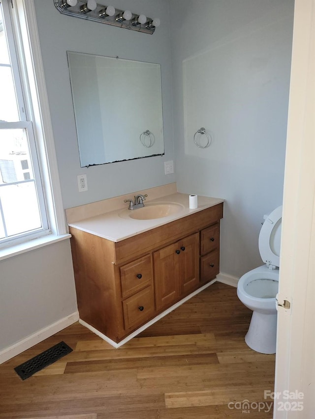 half bath with baseboards, visible vents, toilet, wood finished floors, and vanity