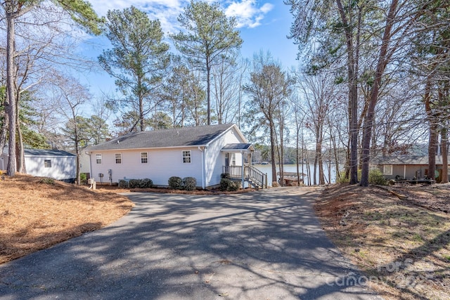 view of side of home featuring driveway, a water view, and an outbuilding