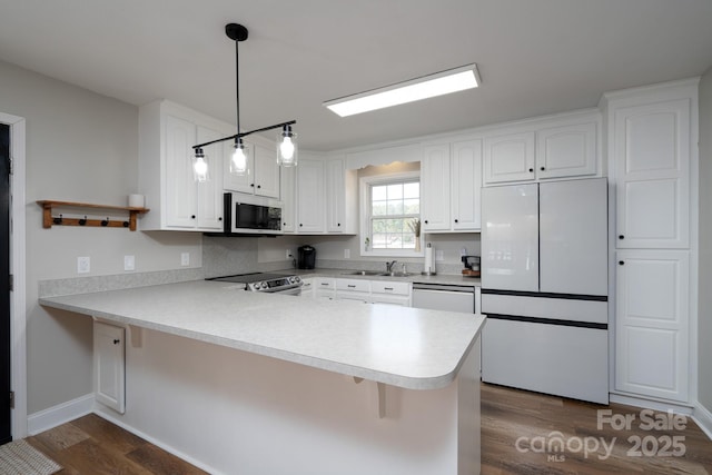 kitchen with dark wood-style floors, white cabinetry, a sink, white appliances, and a peninsula