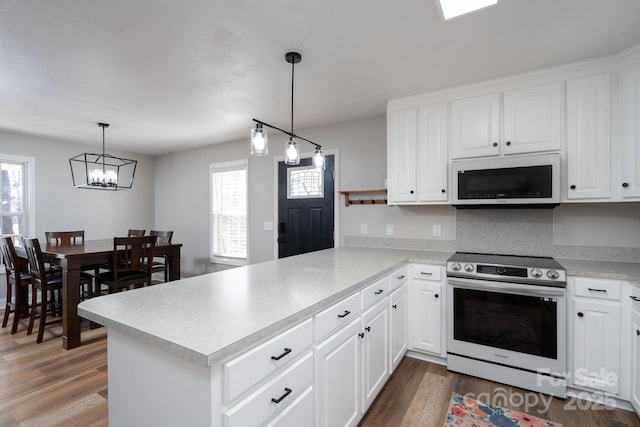 kitchen with a peninsula, white microwave, a wealth of natural light, and stainless steel range with electric cooktop