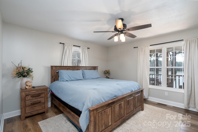 bedroom featuring a ceiling fan, visible vents, baseboards, and wood finished floors