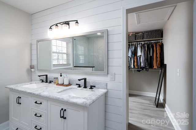 bathroom with double vanity, a spacious closet, a sink, and wood finished floors