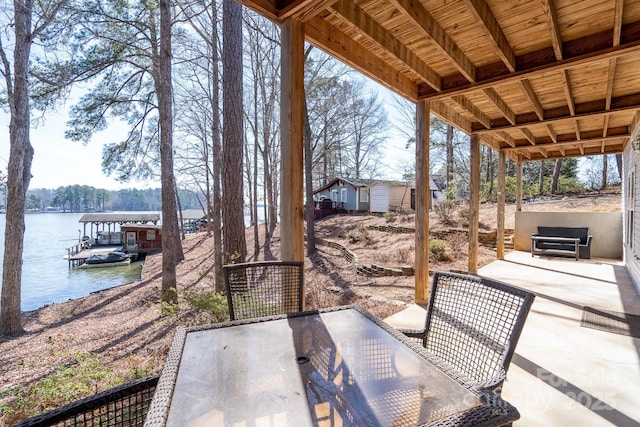 view of patio featuring outdoor dining space, a water view, an outdoor structure, and a dock