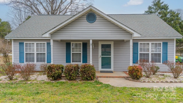 view of front facade with roof with shingles, a porch, and a front yard