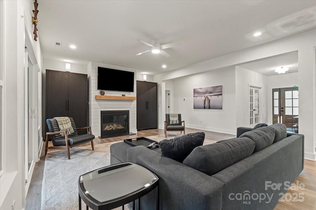 living room with recessed lighting, french doors, a large fireplace, and light wood finished floors