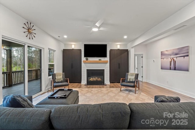 living room featuring a large fireplace, baseboards, recessed lighting, light wood-style flooring, and a ceiling fan