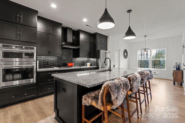 kitchen with appliances with stainless steel finishes, wall chimney exhaust hood, a kitchen breakfast bar, and dark cabinets