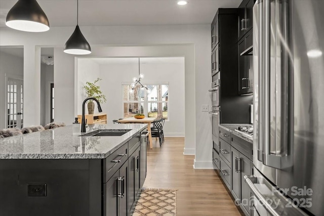 kitchen with light wood-style flooring, a sink, stainless steel appliances, light stone countertops, and hanging light fixtures