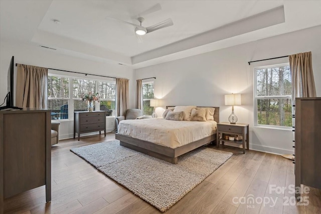 bedroom with light wood-type flooring and a tray ceiling